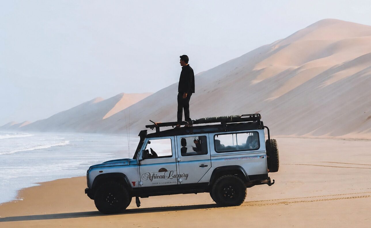 Man staat op het dak van een landrover op het strand nabij Swakopmund
